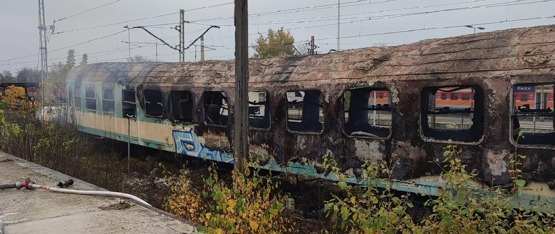 Zdjęcie przedstawia spalony wagon osoby stojący na bocznicy kolejowej