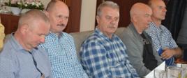 Dzień Strażaka emerytów pożarnictwa. W sali restauracyjnej przy stole siedzą uczestnicy spotkania - 5 mężczyzn. Wszyscy ubrani w cywilne rzeczy. Na stole stoją talerze z surówkami, dzbanki z napojami, filiżanki oraz szklanki