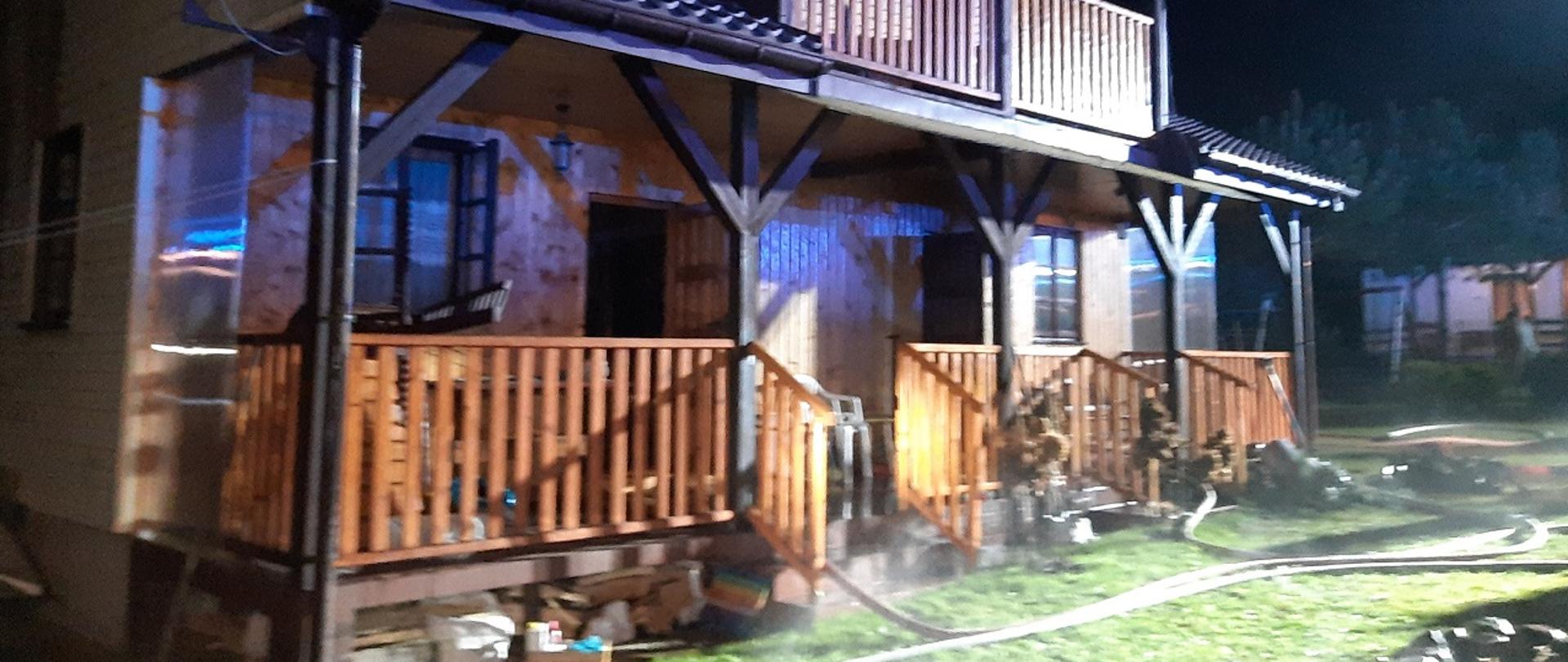 Budynek drewniany z użytkowym poddaszem przed nim leżą węże strażackie.