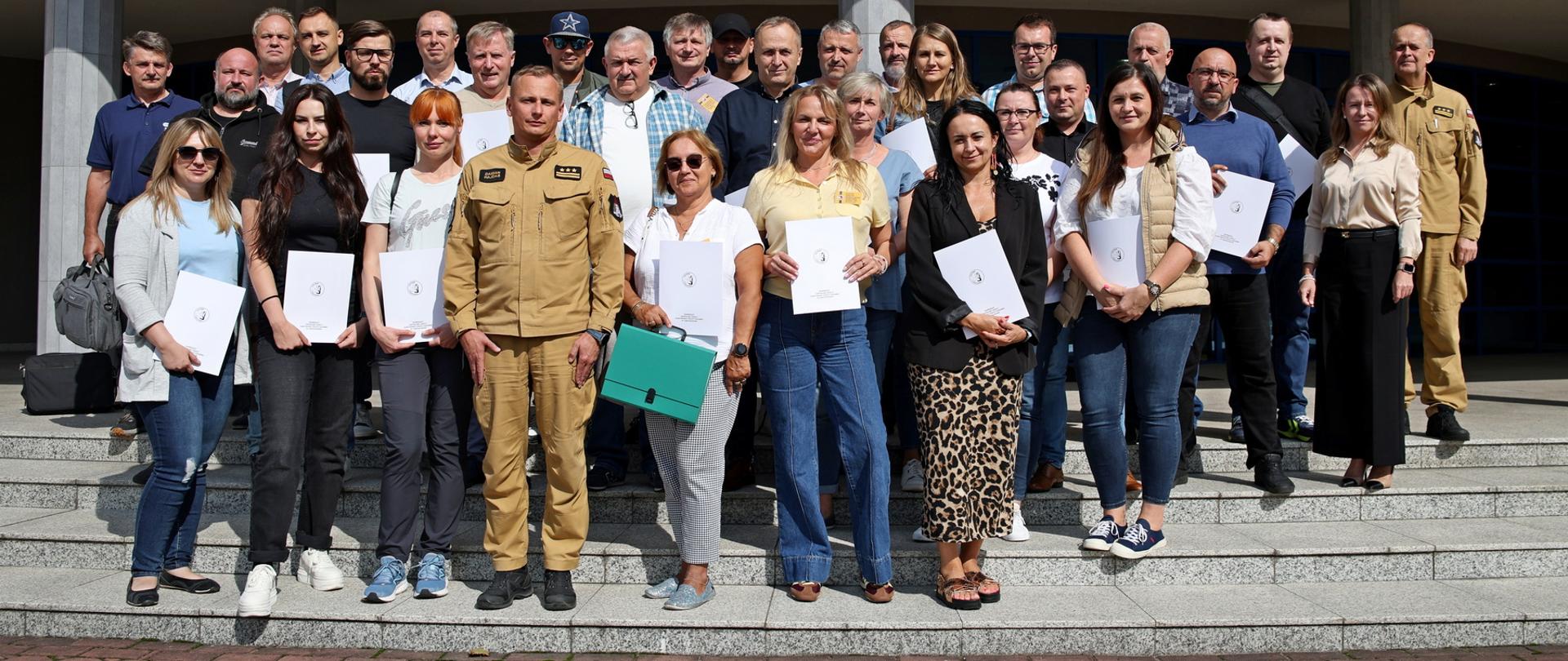 Pamiątkowe zdjęcie grupowe uczestników szkolenia inspektorów ochrony przeciwpożarowej (29 osób) w towarzystwie Zastępcy Komendanta Centralnej Szkoły PSP, kobiety oraz oficera CS PSP
