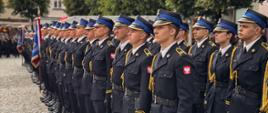 Szereg funkcjonariuszy PSP w galowych mundurach, ustawionych w zwartym szyku na płycie rynku w Poznaniu.
