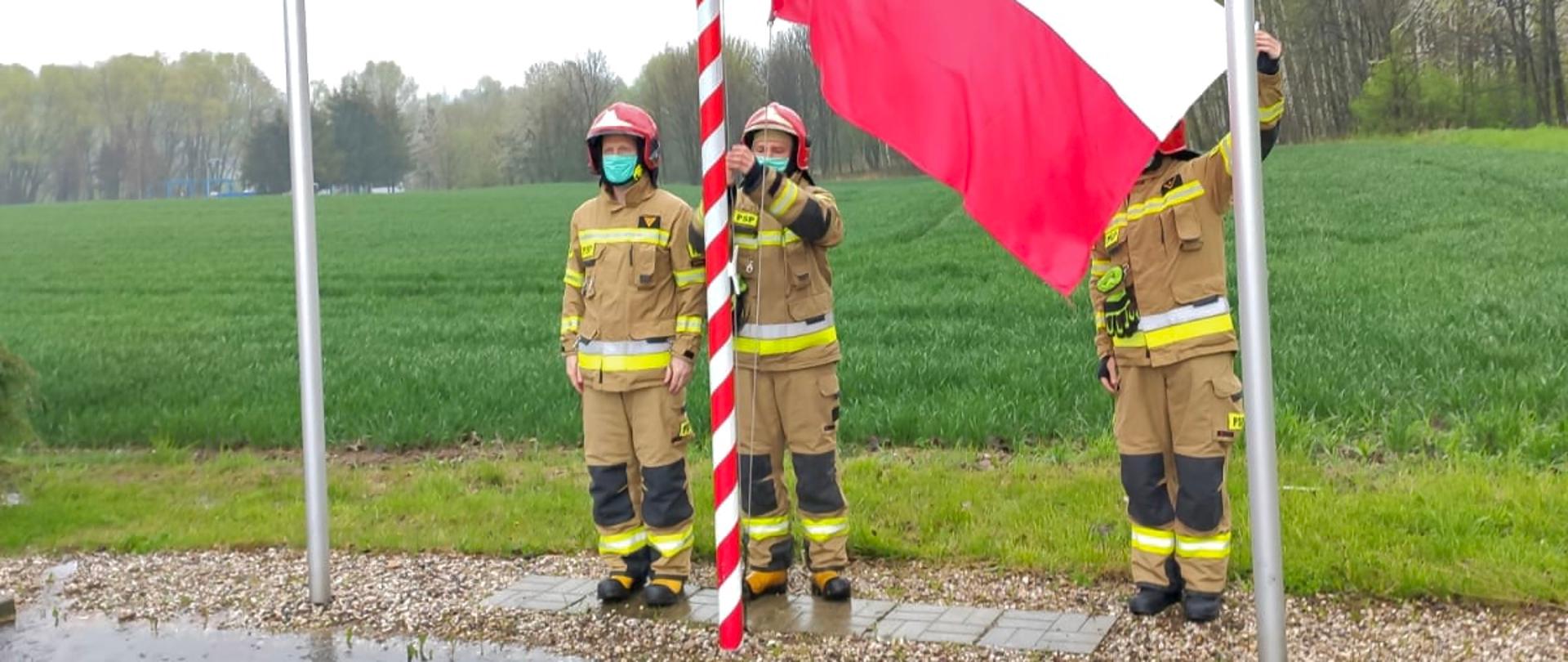 trzech umundurowanych strażaków podczas wciągania flagi na maszt