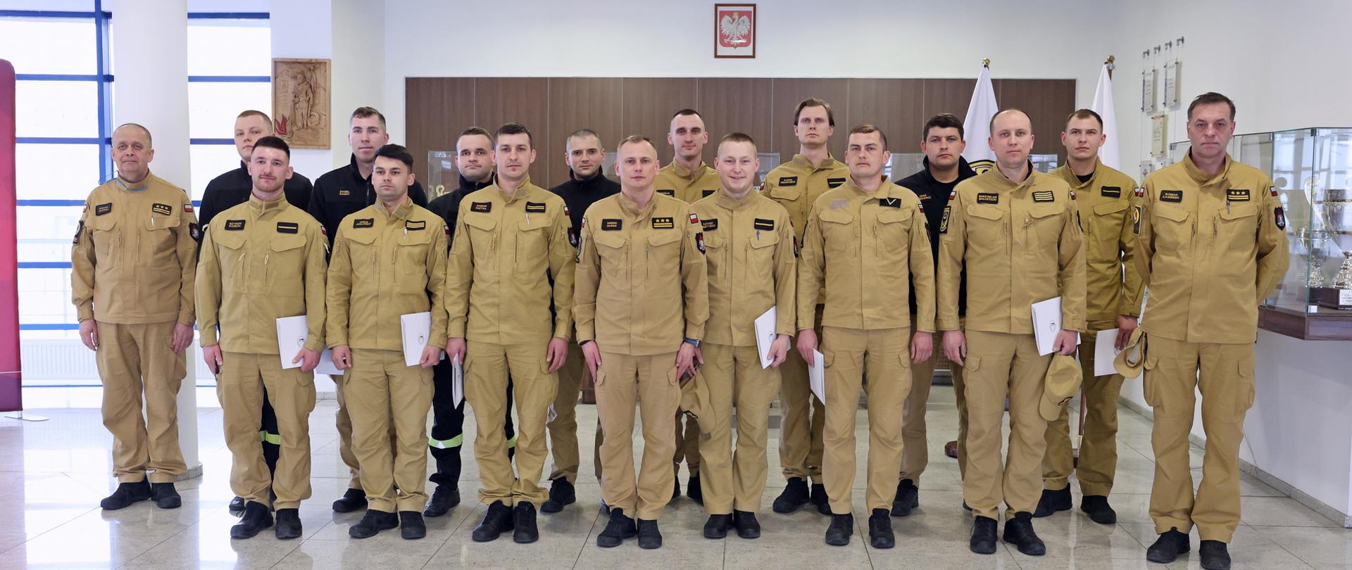 Pamiątkowe zdjęcie grupowe funkcjonariuszy Państwowej Straży Pożarnej będących uczestnikami szkolenia dla kierowców pojazdów uprzywilejowanych (14 osób) w towarzystwie Zastępcy Komendanta Centralnej Szkoły PSP oraz dwóch oficerów CS PSP