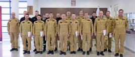 Pamiątkowe zdjęcie grupowe funkcjonariuszy Państwowej Straży Pożarnej będących uczestnikami szkolenia dla kierowców pojazdów uprzywilejowanych (14 osób) w towarzystwie Zastępcy Komendanta Centralnej Szkoły PSP oraz dwóch oficerów CS PSP