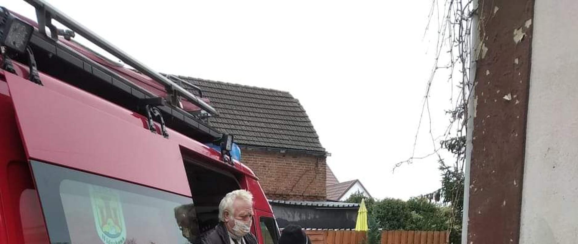 Zdjęcie przedstawia strażaka OSP, który pomaga osobie starszej wysiąść z samochodu