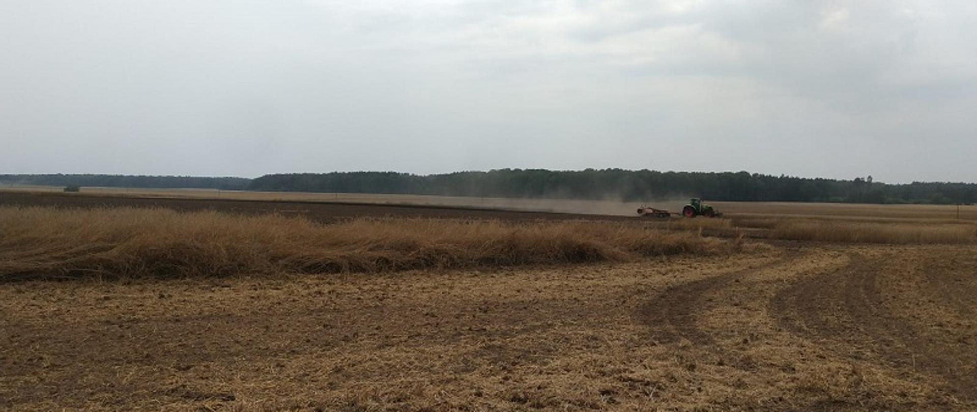 Przedstawia akcję gaśniczą podczas pożaru ścierniska i zboża w miejscowości Liśnica. Na zdjęciu ciągnik rolniczy dokonuje oborania pożarzyska