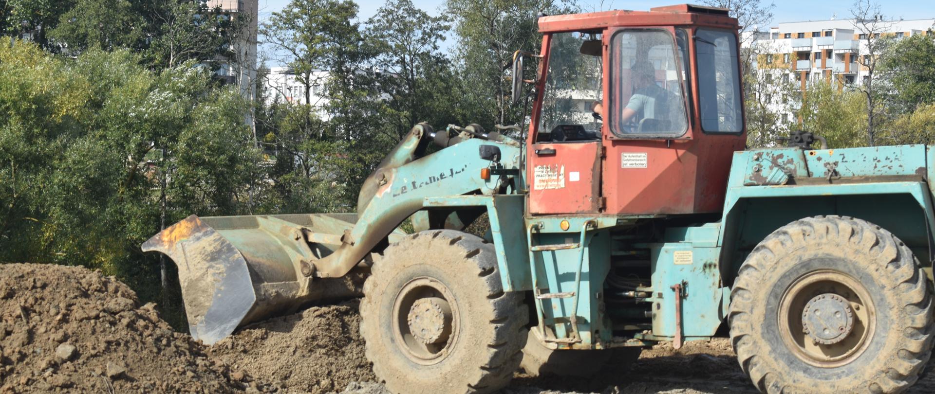 Spychacz stojący na otwartym terenie. Po jego lewej stronie pryzma ziemi.