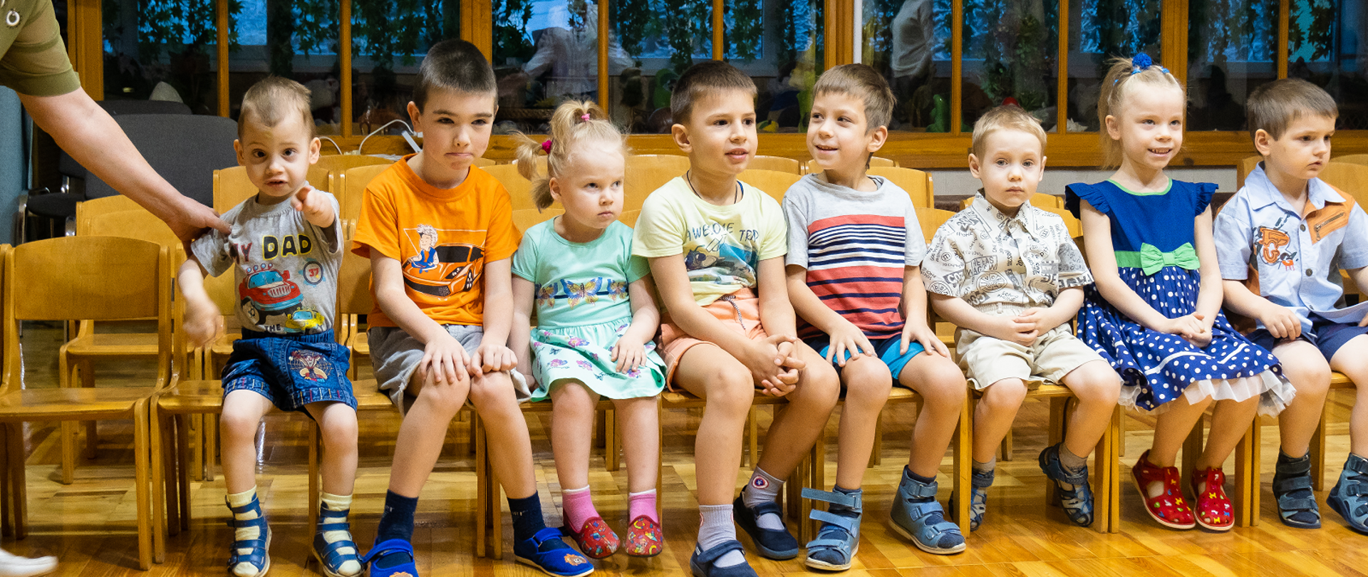 Dzieci w krótkich spodenkach siedzą na krzesłach.