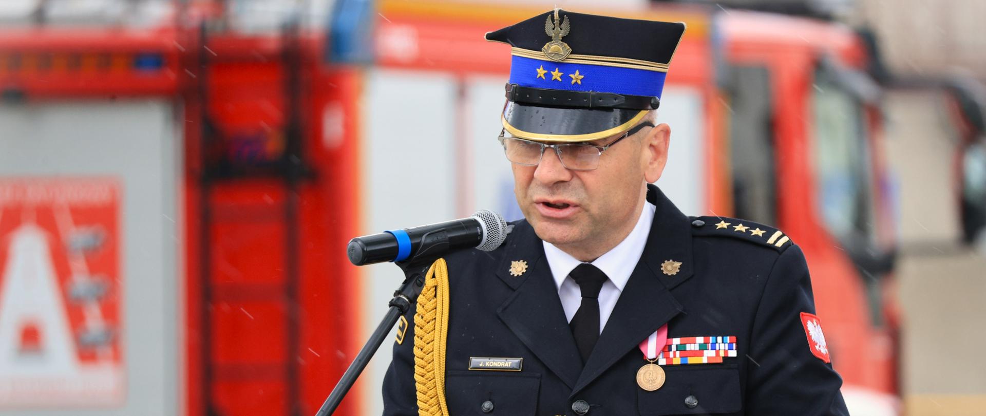 Podlaski komendant wojewódzki PSP - st. bryg. Janusz Kondrat uczestniczył w majowym święcie kolneńskich strażaków - stoi podczas przemówienia przy mównicy, pada deszcz