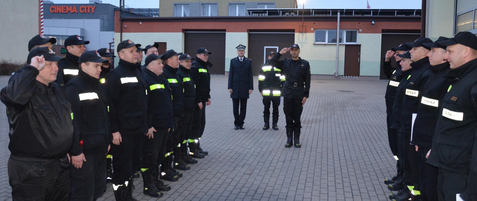 Zdjęcie przedstawia moment zdania służby. Strażacy w dwuszeregu naprzeciw siebie. Z tyłu kierownictwo Komendy. Na pierwszym planie dowódca JRG