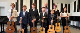 Nauczyciel stoi na scenie ze wszystkimi wykonawcami, którzy trzymają swoje gitary.