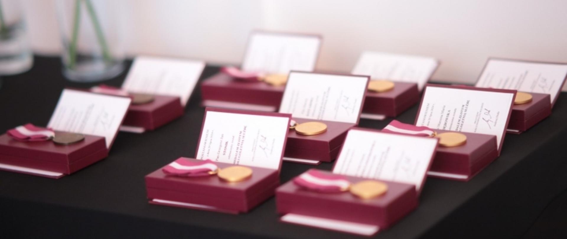 Pudełka z medalami i certyfikatami ułożone na stole w formie oficjalnej ekspozycji.