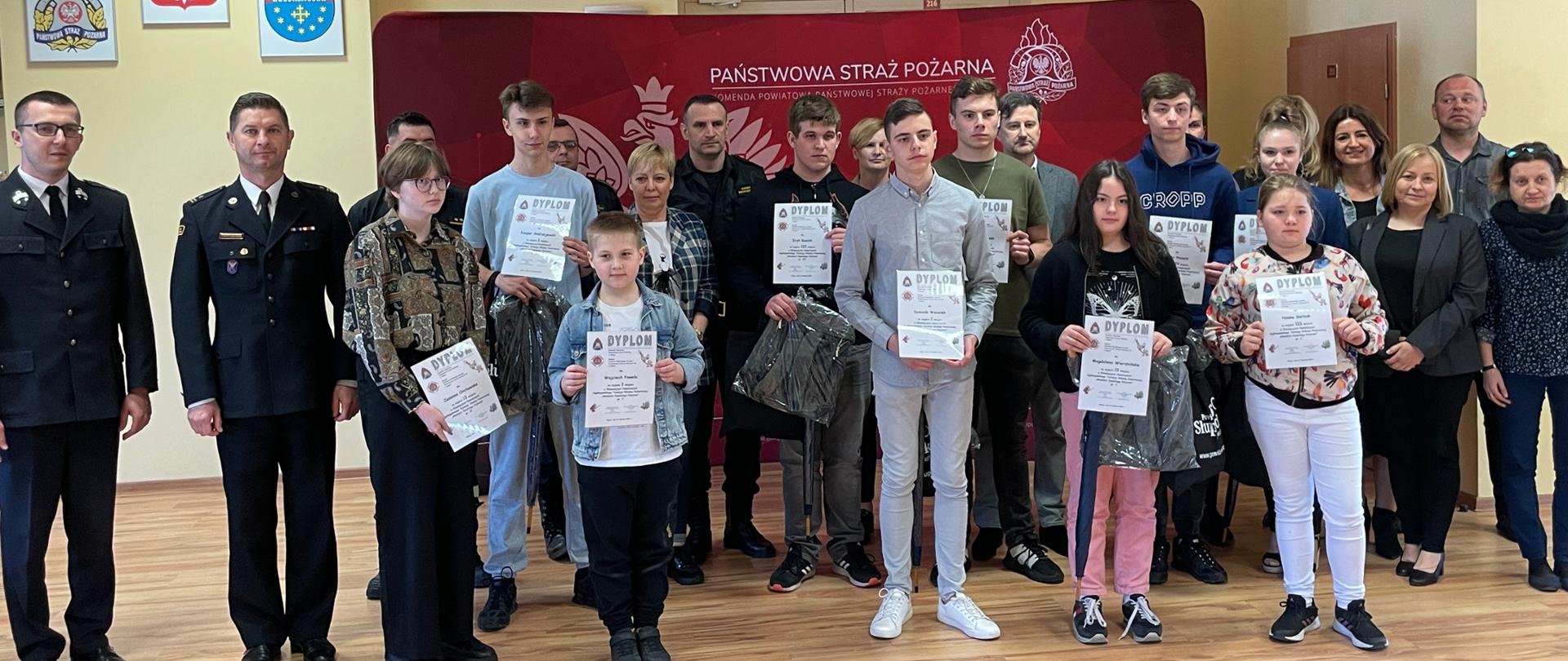 zdjęcie laureatów turnieju oraz funkcjonariusze i opiekunowie uczestników na banerze Komendy Powiatowej PSP w Słupcy