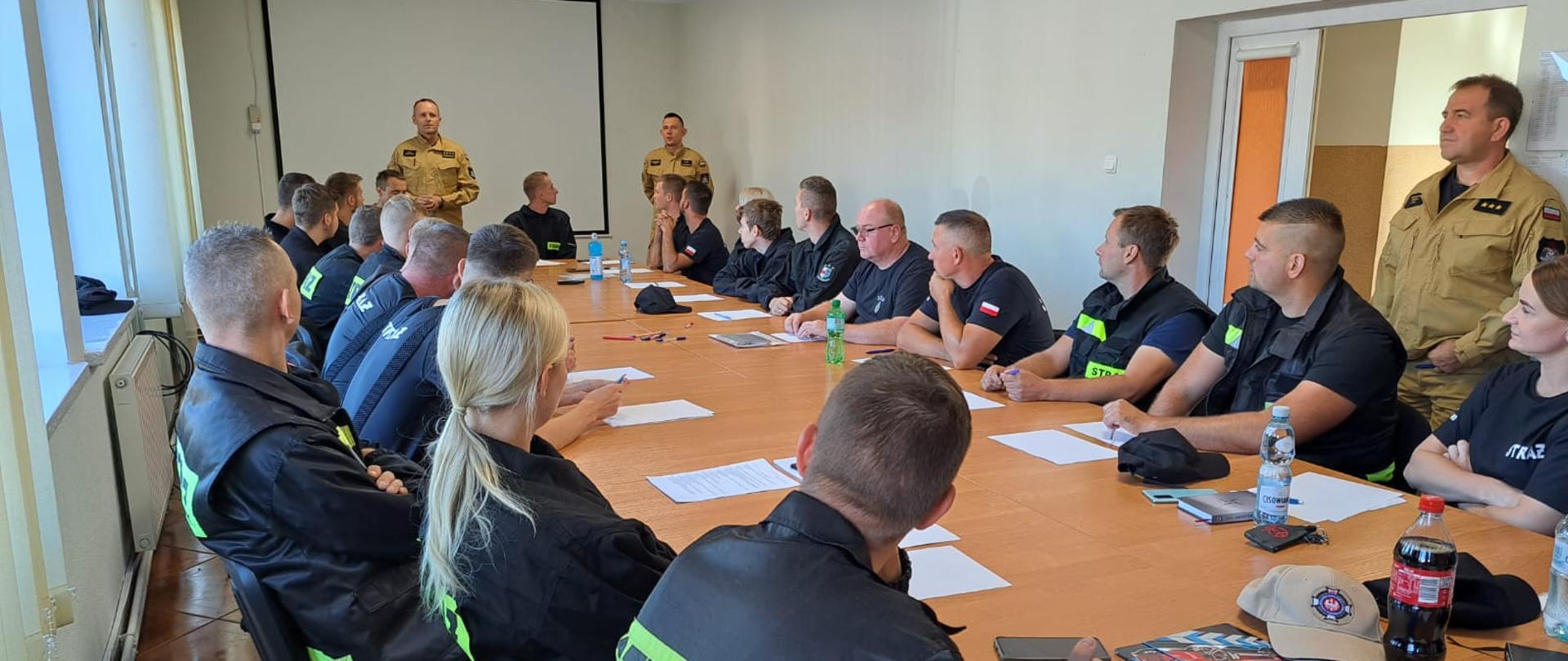 Zdjęcie przedstawia Egzamin teoretyczny szkolenia podstawowego OSP, strażacy siedzą przy stalach i rozwiązują test.