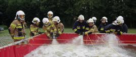 Widok z przodu. Strażacy ratownicy OSP napełniają bufor wodny. 