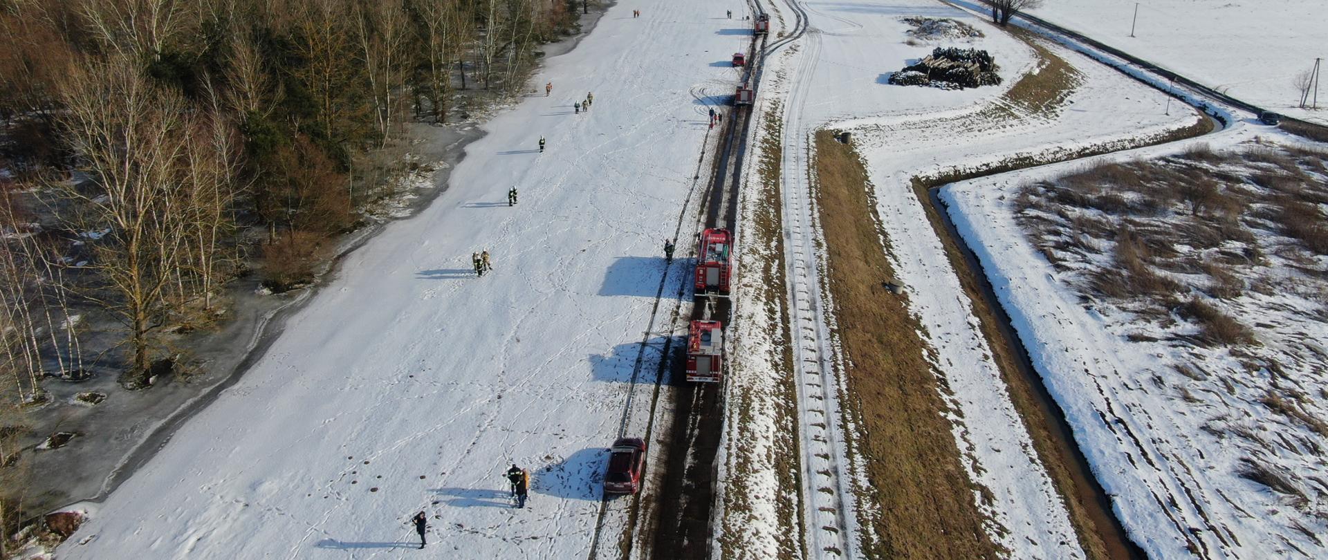 Na zdjęciu widać strażaków i samochody na śniegu.