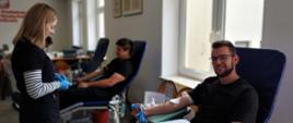 Na zajęciu widoczni dwaj mężczyźni jeden w czarnej koszulce i czarnych spodniach drugi w koszulce i spodniach koloru czarnego siedzący na krzesłach na sali podczas oddawania krwi podczas akcji zbiórki krwi zorganizowanej przez Klub Honorowych Dawców Krwi Polskiego Czerwonego Krzyża przy Komendzie Powiatowej Państwowej Straży Pożarnej w Gorlicach