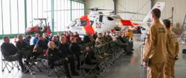 Hangar lotniczy z siedzącymi na krzesłach uczestnikami ćwiczeń w trakcie zajęć warsztatowych. Przed nimi stoi czterech oficerów i przedstawia założenia. 