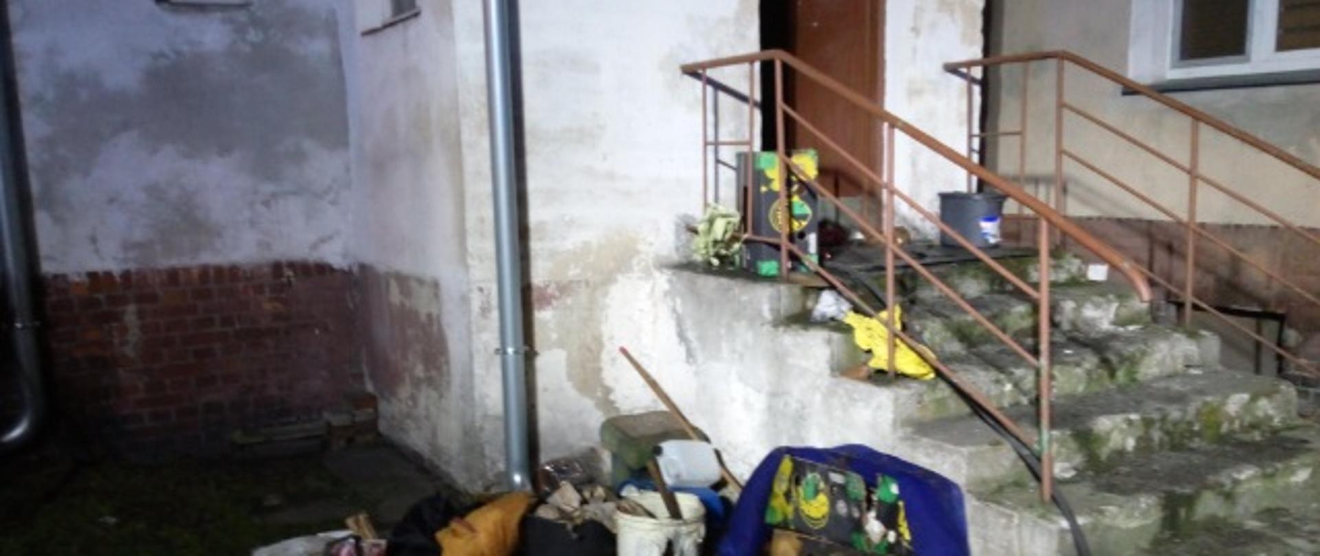 Na zdjęciu widać wejście do budynku, po schodach i porozrzucane rzeczy w okolicy
