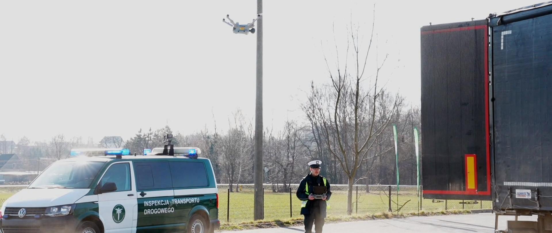 Kadr z filmu - inspektor ITD, sterujący dronem, dron, inspekcyjny furgon i ciężarówka na przydrożnym parkingu
