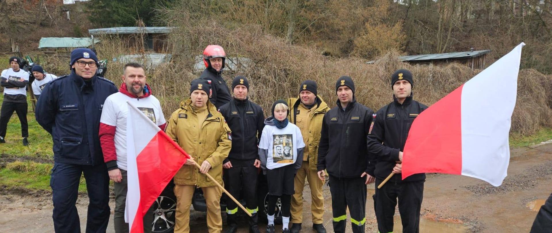Na zdjęciu grupa strażaków, trzymają w rekach dwie flagi Polski.