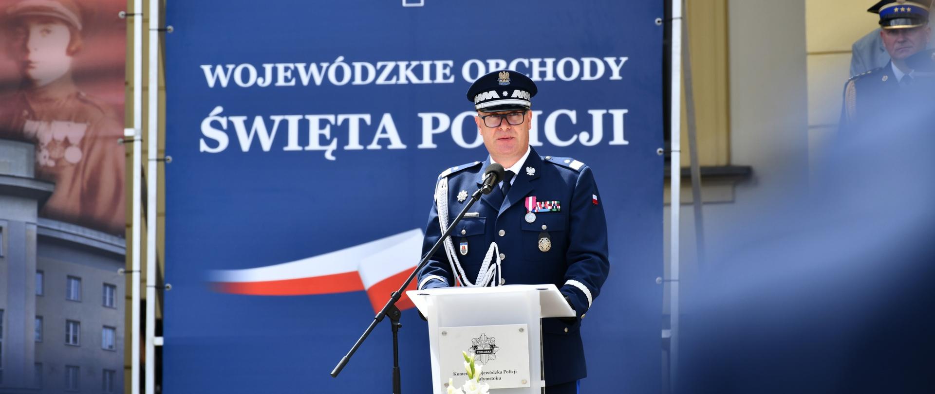Komendant wojewódzki Policji w Białymstoku podczas przemówienia, w tle baner z logo Policji