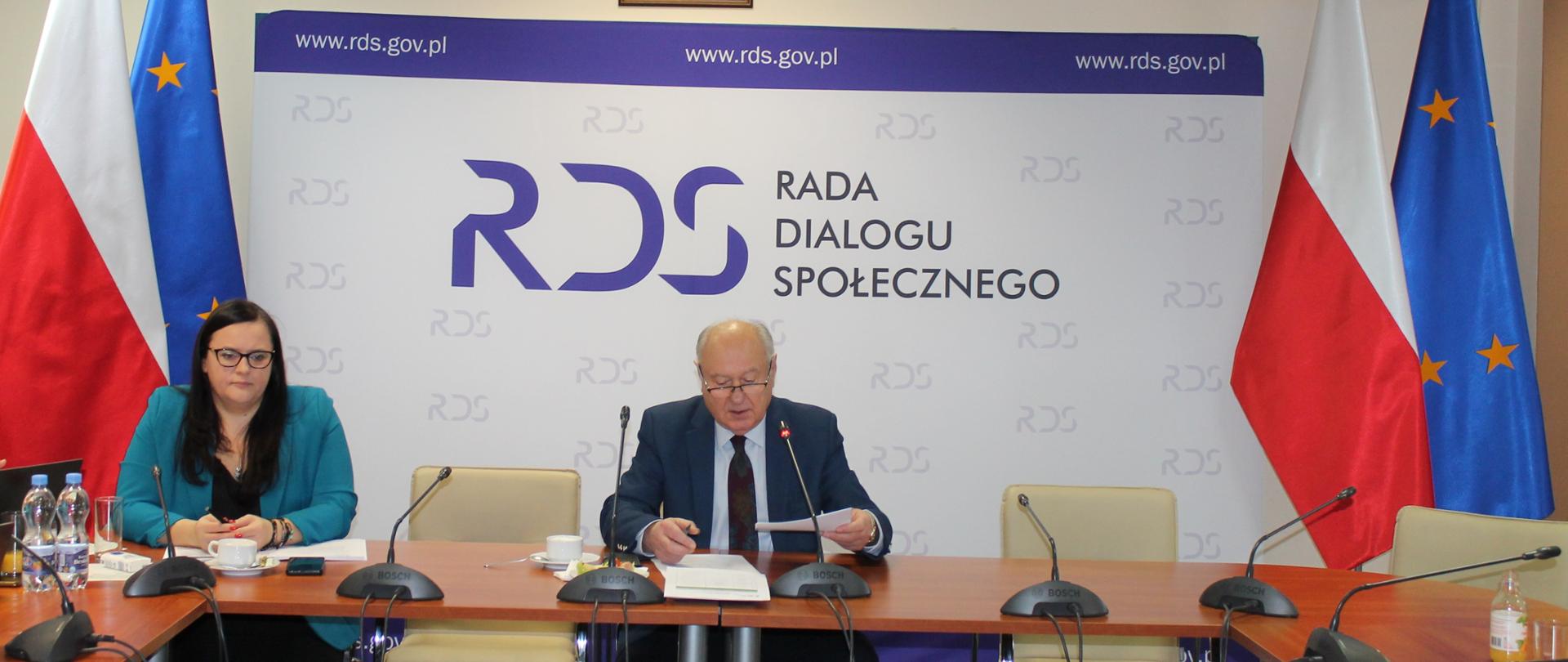 Zdjęcie przedstawia stół prezydialny za którymi siedzi: Małgorzata Jarosińska-Jedynak – Sekretarz Stanu w Ministerstwie Funduszy i Polityki Regionalnej oraz Jan Klimek – Przewodniczący Zespołu. W tle osób baner z napisem Rada Dialogu Społecznego. Po lewej i prawej stronie stoją po dwie flagi: Polski i UE. Nad banerem wisi godło Polski.