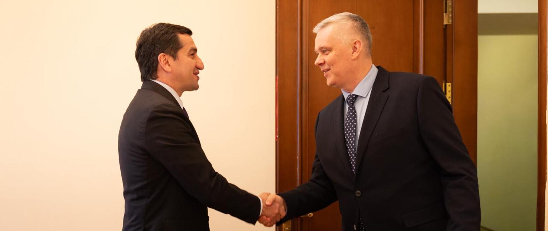 Na zdjęciu witający się ze sobą doradca prezydenta ds. zagranicznych Hikmet Hajiyev (po lewej stronie) i minister Tomasz Siemoniak (po prawej). W tle zdjęcia, po prawej stronie otwarte brązowe drzwi. Po lewej stronie widać fragment krzesła.
