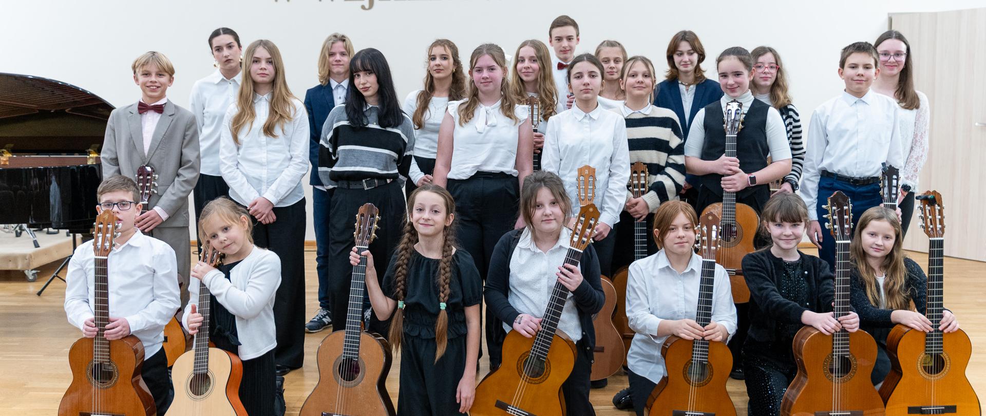 Na sali koncertowej pozują z gitarami stojąc uczniowie z klasy Zofii Marszk i Piotra Kłosowskiego