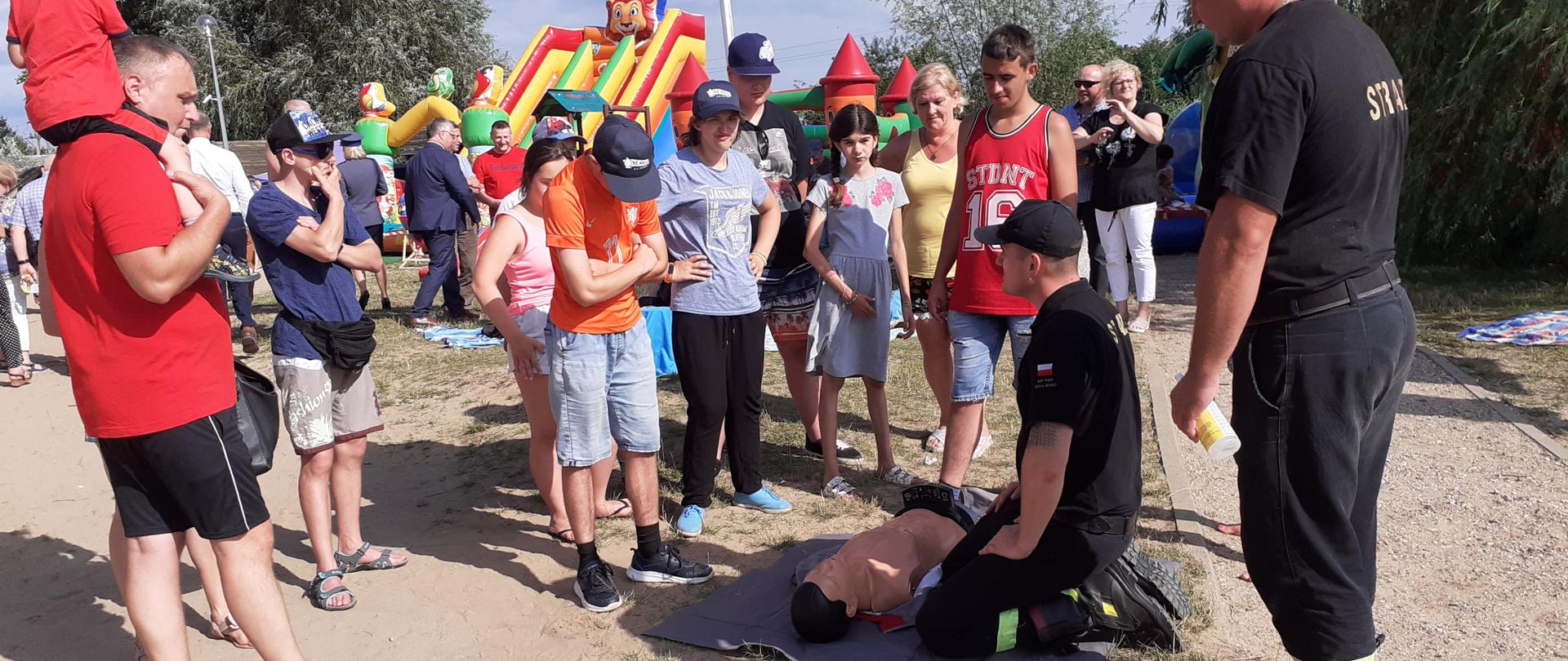 Strażacy PSP pokazują grupie ludzi jak udzielać pierwszej pomocy.