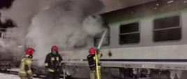 Trzech strażaków gasi pożar wagonu, duże zadymienie.