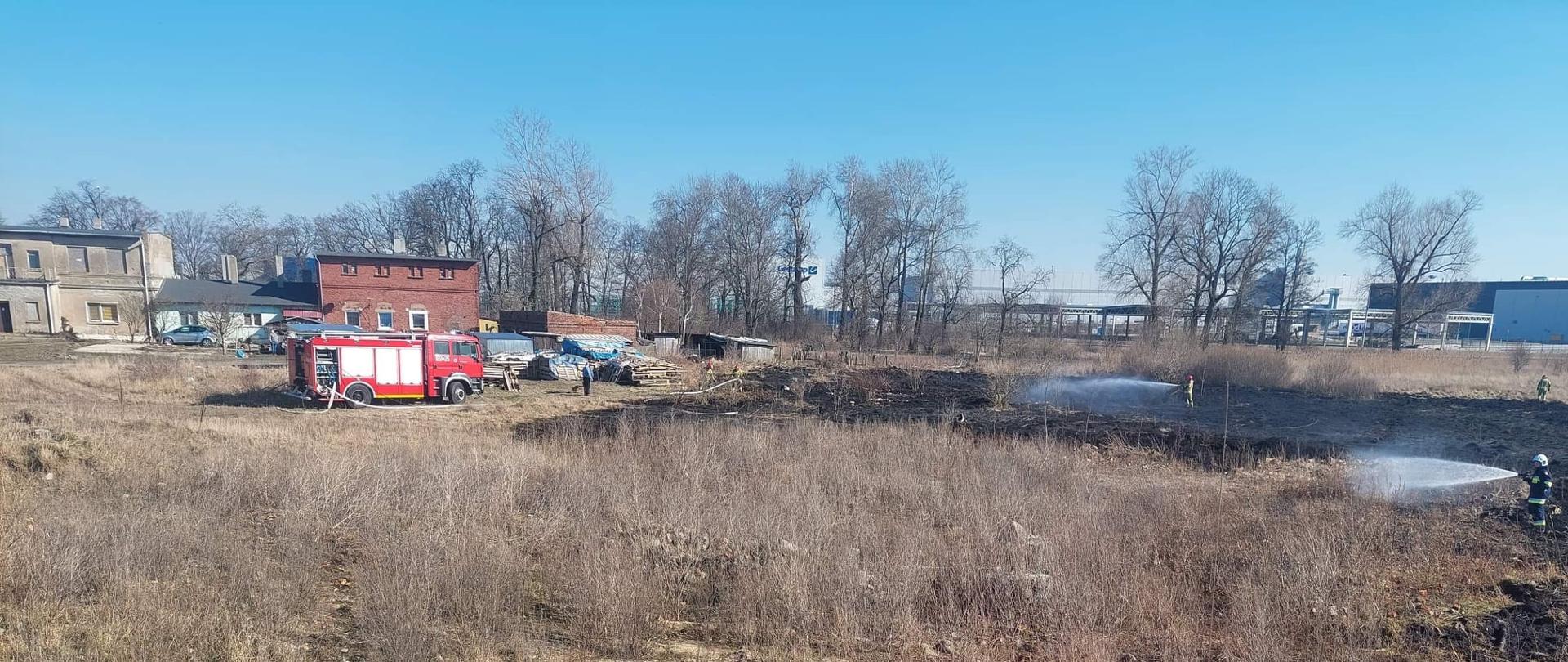 Zdjęcie przedstawia zdjecie z dachu wozu strażackiego i strażaków gaszących trawę