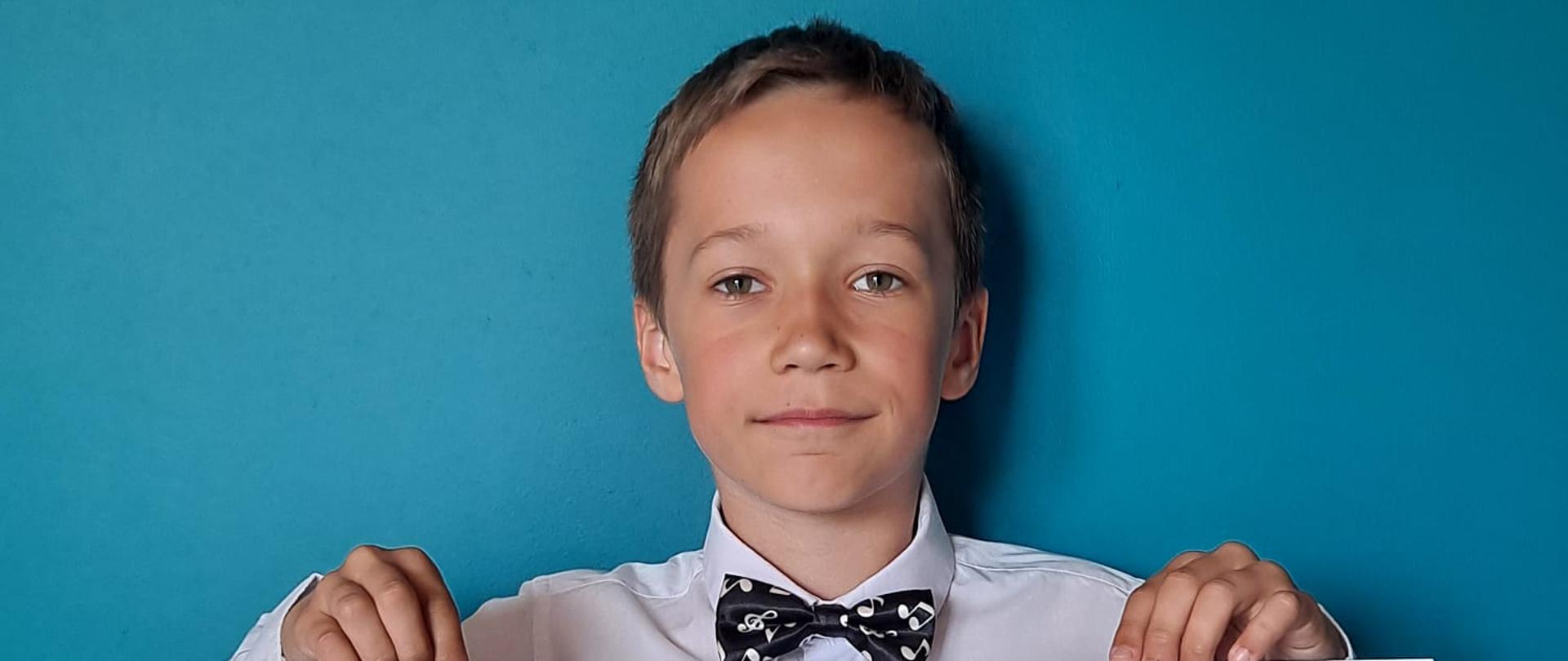 Chłopiec elegancko ubrany trzyma w rękach dwa dyplomy wyróżnienia i dla najmłodszego uczestnika w XIV Konkursie Wiedzy o Życiu i Twórczości Kompozytorów: prof. Józef Świder, Jastrzębie-Zdrój, 22.05.2023 r.