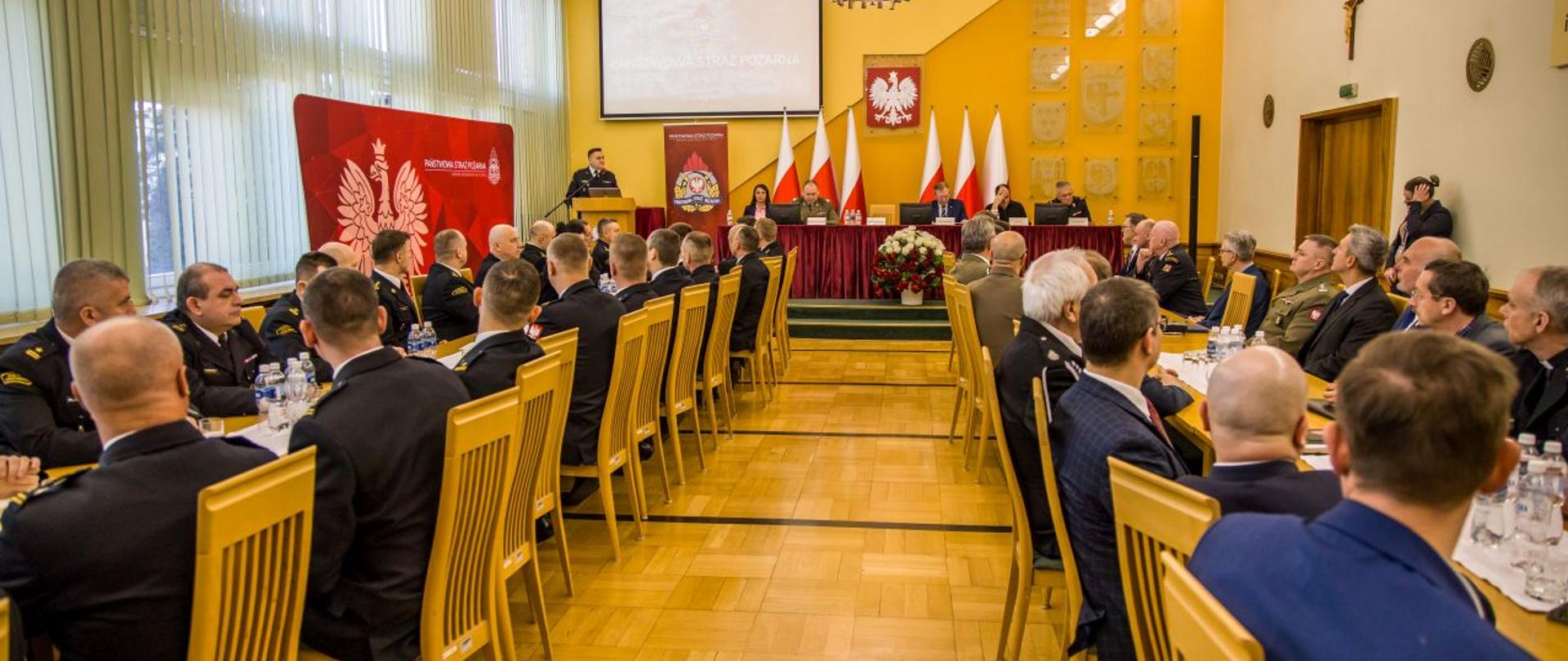 St. bryg. Krzysztof Kędryk Opolski Komendant Wojewódzki PSP przemawia podczas narady rocznej kadry kierowniczej PSP województwa opolskiego. W tle widoczny roll-up z logiem PSP oraz napisem na górze koloru białego: Państwowa Straż Pożarna oraz poniżej Komenda Wojewódzka PSP w Opolu. Po lewej stronie stoły prostopadle ustawione do stołu prezydialnego, przy których siedzą Komendanci Powiatowi i Miejski PSP wraz ze swoimi Zastępcami. Po prawej stronie stoły prostopadle ustawione do stołu prezydialnego, przy których siedzą zaproszeni goście i komendanci służb współpracujących. Narada w sali im. Prezydenta Lecha Kaczyńskiego w Opolskim Urzędzie Wojewódzkim w Opolu.