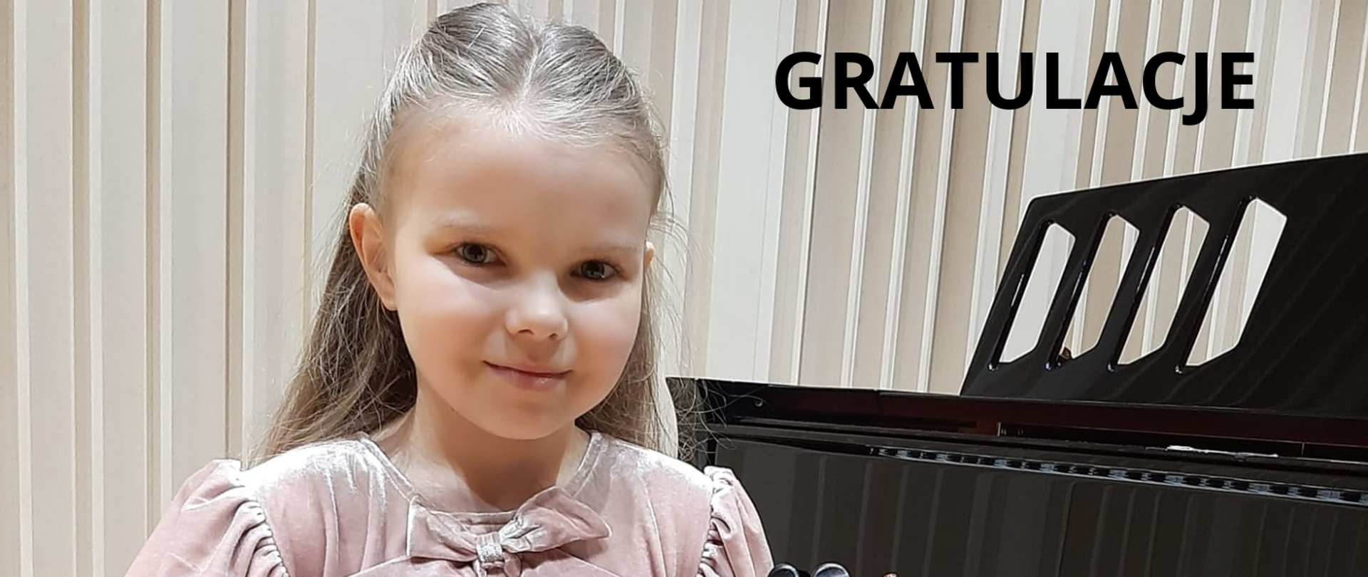 Na zdjęciu po lewej stronie dziewczynka w jasnej sukience i blond włosach. po lewej stronie widać fragment czarnego fortepianu. Nad nim czarny napis: "gratulacje". Tło obrazka w odcieniach brązu.