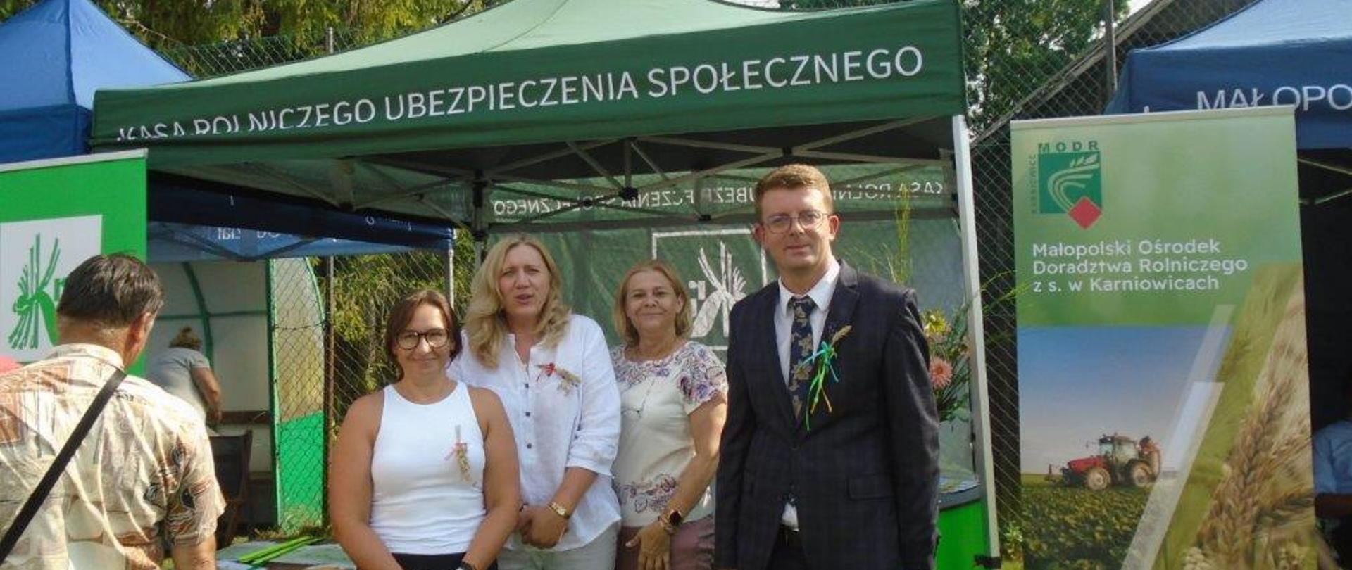 Na tle stoiska informacyjnego KRUS stoją trzy kobiety oraz mężczyzna 