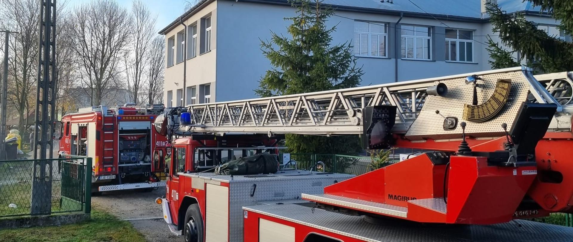 Zdjęcie przedstawia zaparkowane pojazdy pożarnicze w bramie wjazdowej do Niepublicznego Młodzieżowego Ośrodka Wychowawczego.