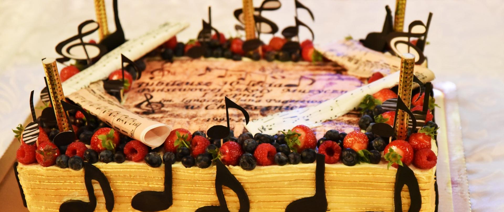 Duży prostokątny tort jubileuszowy ozdobiony owocami i nutami 3D