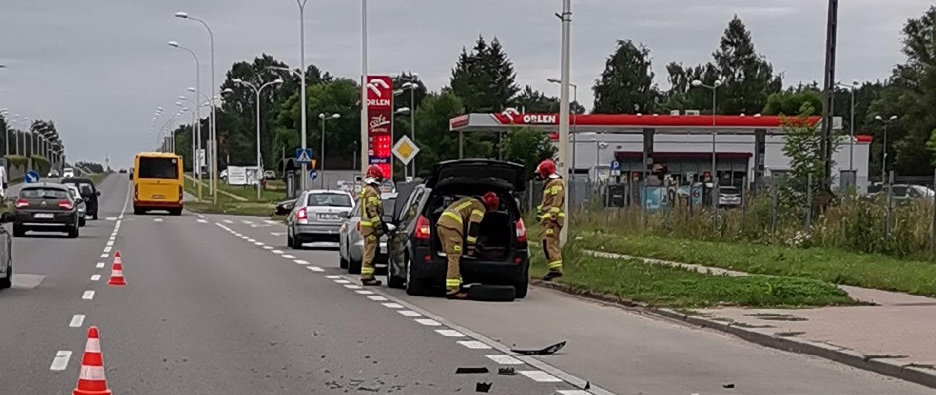 Zdjęcie przedstawia ulicę Krakowską. Po prawej stronie, na poboczu stoją uszkodzone samochody osobowe. Przy nich trzech strażaków. 