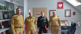 Na zdjęciu widoczni są komendant powiatowy, jego zastępca oraz dowódca jednostki ratowniczo-gaśniczej w Ustrzykach Dolnych, którzy ubrani są w mundury piaskowe oraz strażak w ubraniu koszarowym który trzyma w rękach decyzje o awansie. Zdjęcie wykonane w pomieszczeniu. 