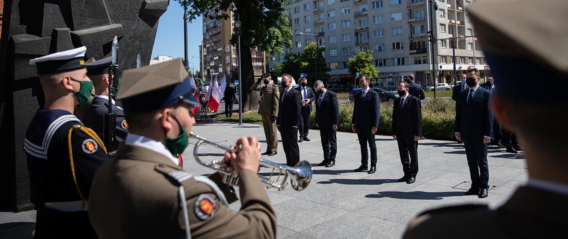 Andrzej Duda Prezydent RP w towarzystwie m.in. Mariusza Kamińskiego Ministra MSWiA, Mariusza Błaszczaka Ministra Obrony Narodowej, Pawła Solocha Szefa BBN Pawła Solocha i płk Szczepana Głuszczaka Dyrektora Centrum Weterana Działań poza Granicami Państwa składa wieniec przed pomnikiem Żołnierzy Poległych w Misjach i Operacjach Wojskowych poza Granicami Państwa. Na pierwszym planie widać Trębacza Orkiestry Reprezentacyjnej WP i Asystę Honorową.