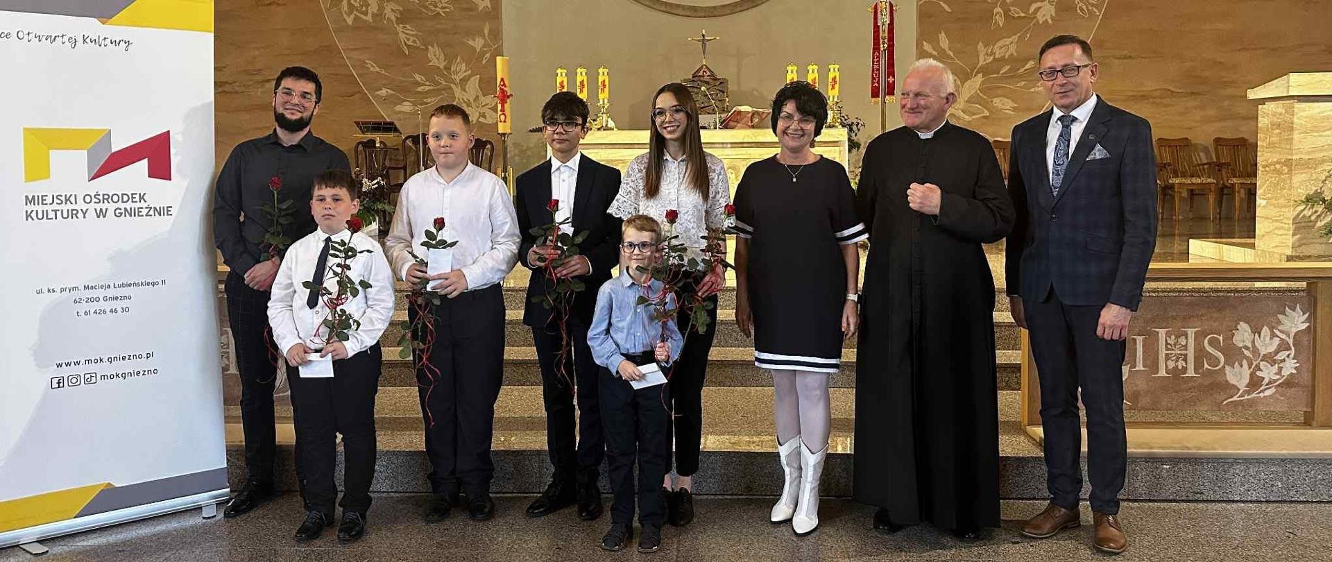 Uczniowie i osoby dorosłe przed ołtarzem w kościele.