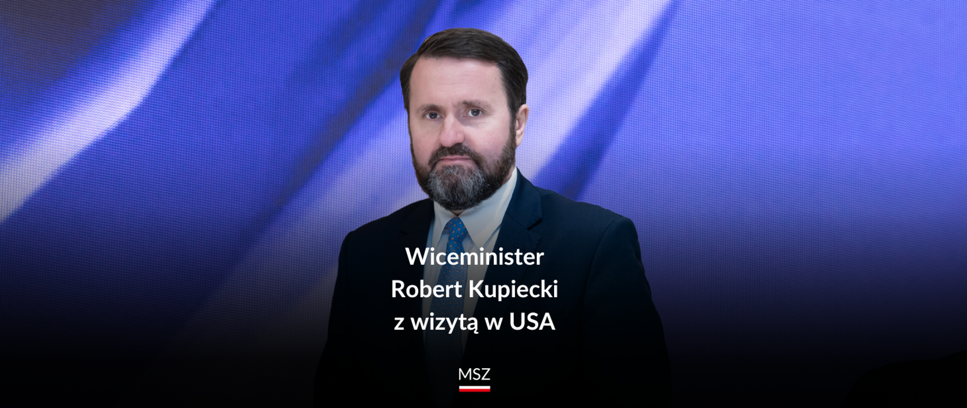 Grafika przedstawiająca portret mężczyzny z brodą z napisem: Wiceminister Robert Kupiecki z wizytą w USA.
Pod napisem widać napis MSZ oraz pod nim flagę Polski.