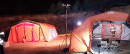 Widoczne namioty w porze nocnej ustawione prze strażaków wraz z oświetleniem wyposażeniem i nagrzewnicami