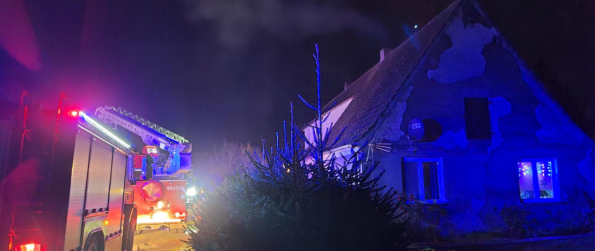 Widoczny budynek 2 rodzinny oraz pojazdy gaśnicze i podnośnik hydrauliczny