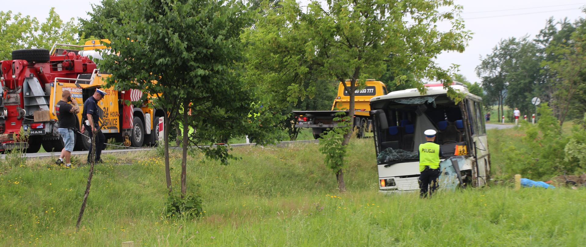Wypadek na DK45 w Jełowej. Na zdjęciu po prawej stronie autobus w rowie. Autobus zdewastowany - po wypadku. Po lewej stornie kadru straż pożarna oraz fragment drogi.