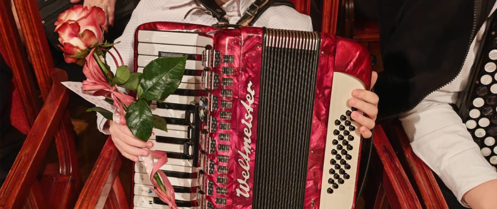 Dziewczynka siedzi na widowni z akordeonem i różą.
