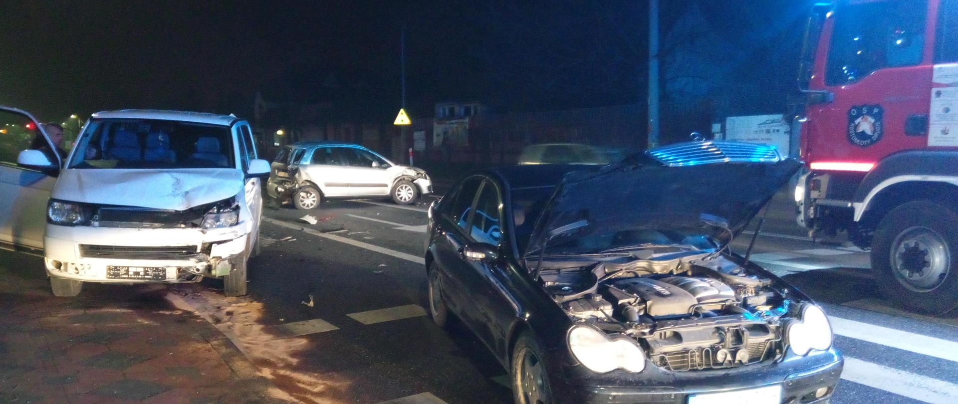 Zdjęcie przedstawia samochody biorące udział w zdarzeniu: Suzuki SX4, Mercedes C-klasa i Volkswagen Transporter na drodze nr 74 w miejscowości Kostomłoty Drugie oraz fragment samochodu pożarniczego OSP Kostomłoty 319-31 GBA-Rt 3,5/16 Man.