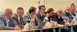 grupa oficjeli, w tym wicewojewoda, siedzą przy stole, wicewojewoda przemawia przez mikrofon
