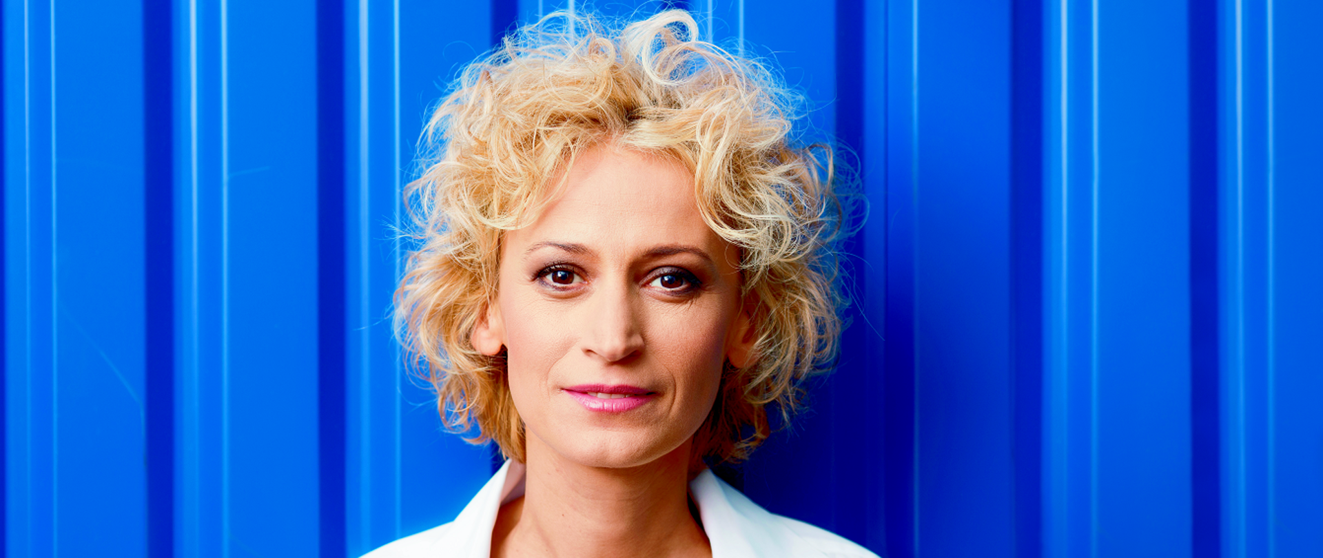 On a blue background, a woman with blond hair dressed in a white shirt